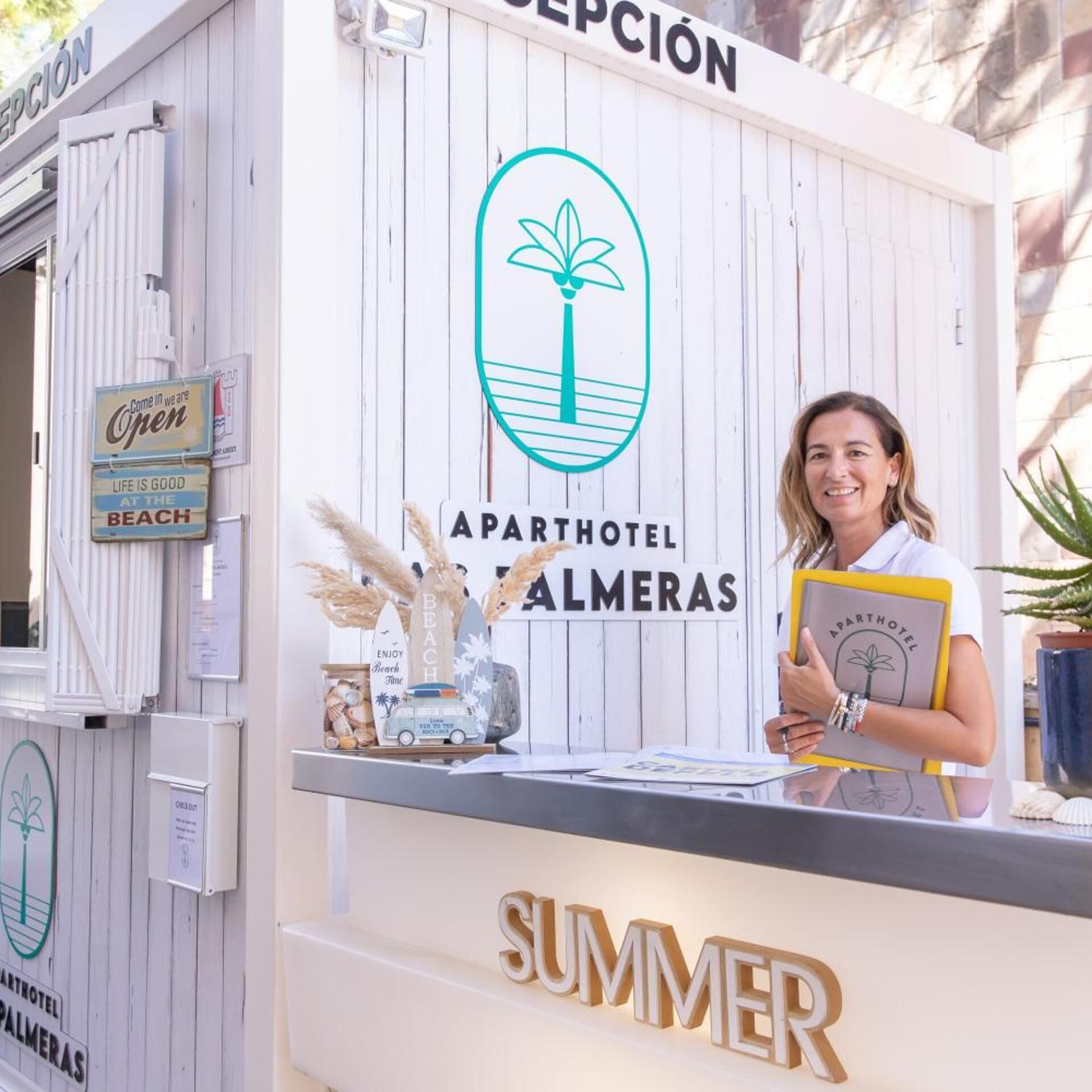Un quiosco de madera blanca con el texto 'APARTHOTEL PALMERAS' y un logotipo con una palmera.