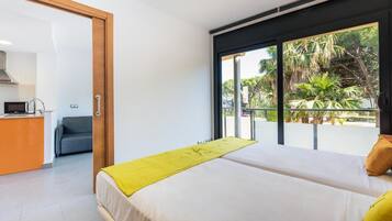 Una habitación de hotel moderna con una cama, un escritorio pequeño y vistas a palmeras a través de amplios ventanales.