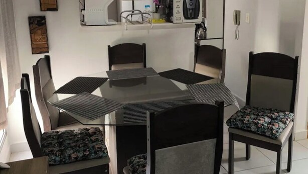 Un comedor con una mesa rectangular, seis sillas, una cocina con armarios, un refrigerador y una máquina de café.
