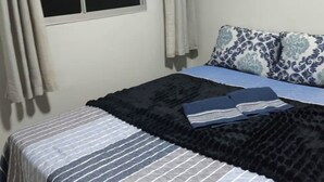 Un dormitorio con cama, ventana con cortinas y almohada estampada.