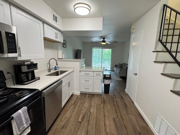 A modern kitchen with a microwave, coffee maker, and stove. There's a window with a view of greenery and a ceiling fan.