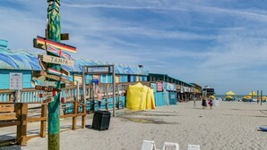 A beach with a signpost indicating directions to various locations, a yellow tent, and a sign for Cocoa Beach Pier. - Tropical 2 Bed Beach Villas Unit A (Cocoa Beach)
