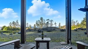 A wooden table with two glasses of wine and a bottle, set on a gravel area with wooden benches. - Pacific Seas Suite-Wild Pacific Trail, Ocean View! (Ucluelet)