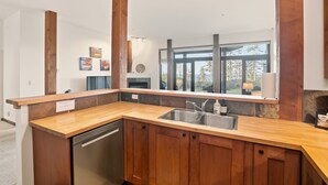 A modern kitchen with wooden cabinets, a stainless steel sink, and a large window offering a view of trees. - Pacific Seas Suite-Wild Pacific Trail, Ocean View! (Ucluelet)
