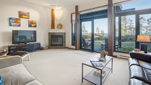 A modern living room with a fireplace, large windows, and artwork on the walls. - Pacific Seas Suite-Wild Pacific Trail, Ocean View! (Ucluelet)