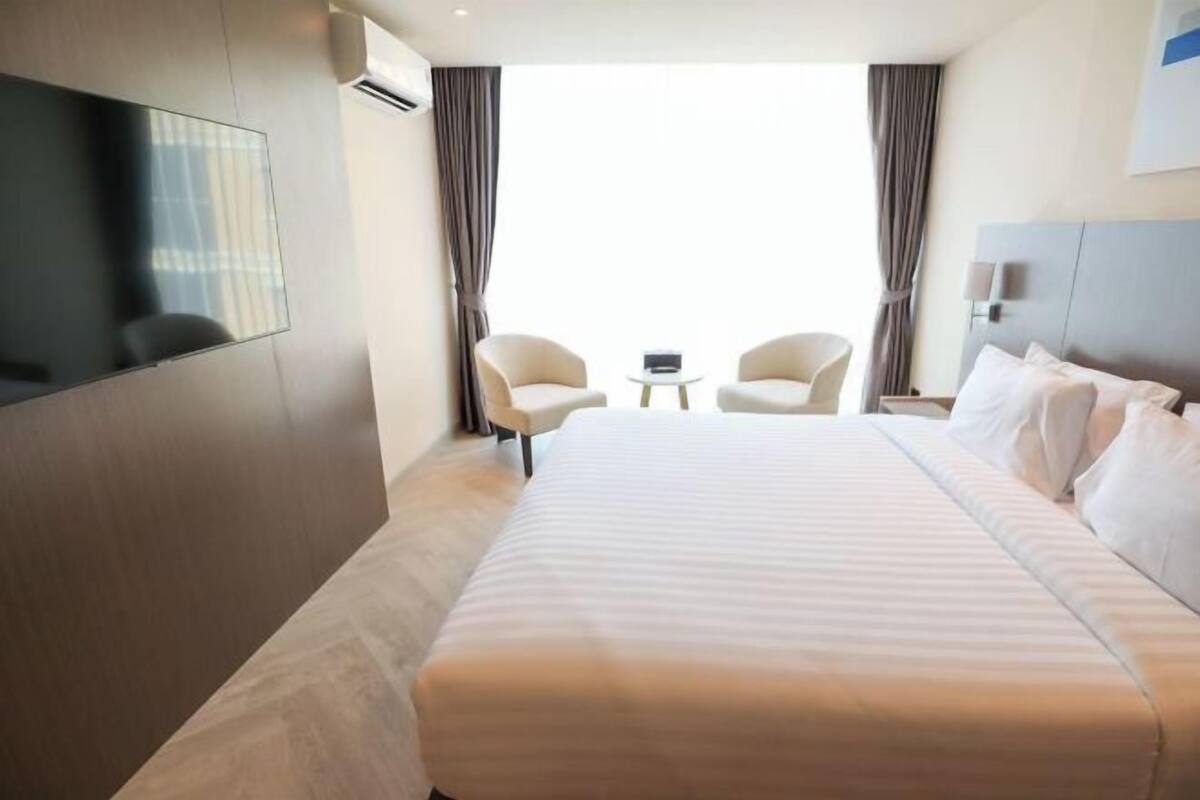 Habitación de hotel con una cama grande, dos sillones, una mesita y un televisor montado en la pared.