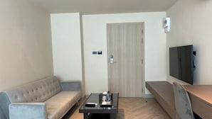 A modern living room with a grey sofa, a coffee table, a TV mounted on the wall, and a wooden door. - The One Cozy Living (Pattaya)