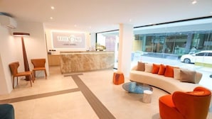 A modern hotel lobby with a reception desk, seating area, and a view of the street outside. - The One Cozy Living (Pattaya)