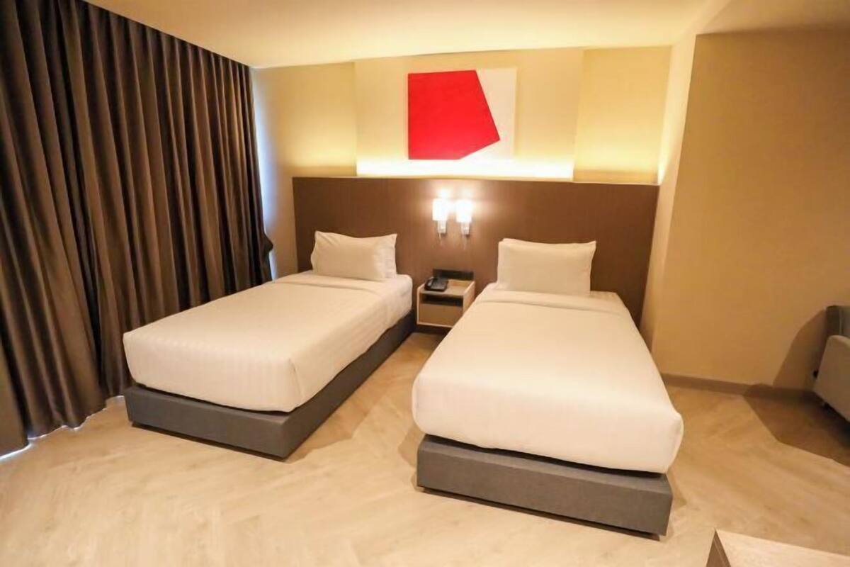 Habitación de hotel con dos camas, una mesita de noche, una pared de acento roja y una cortina.