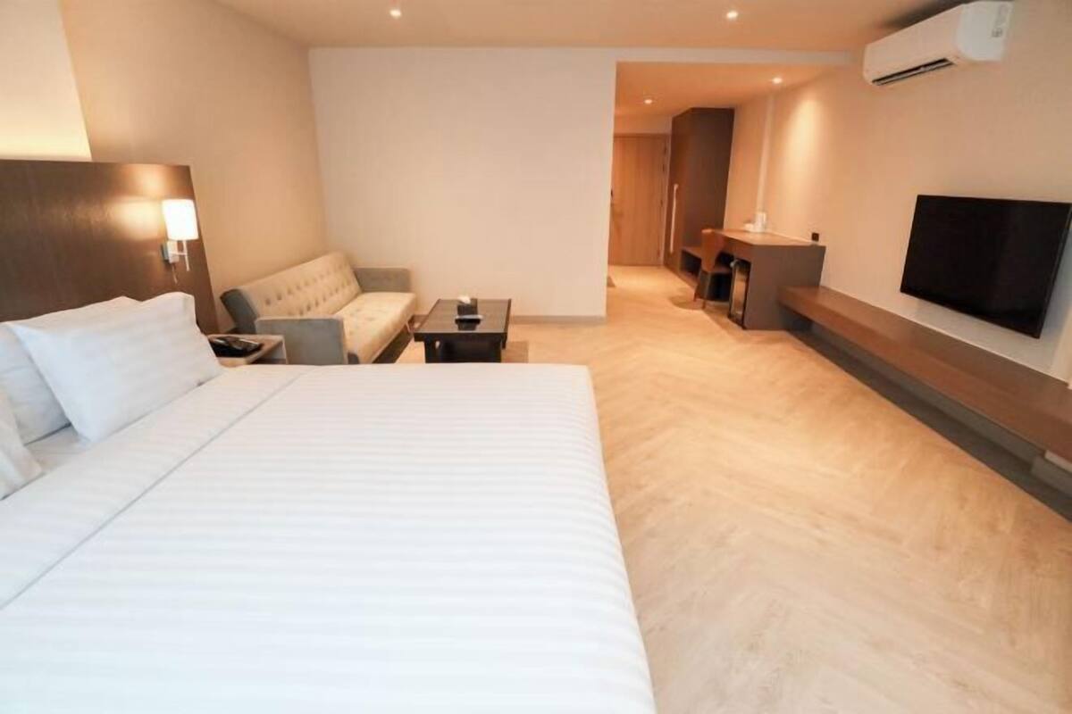 Habitación de hotel con una cama grande, un sofá, una mesita, un televisor y un escritorio.
