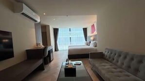 A modern hotel room with a flat-screen TV, a sofa, a bed, and a coffee table. - The One Cozy Living (Pattaya)