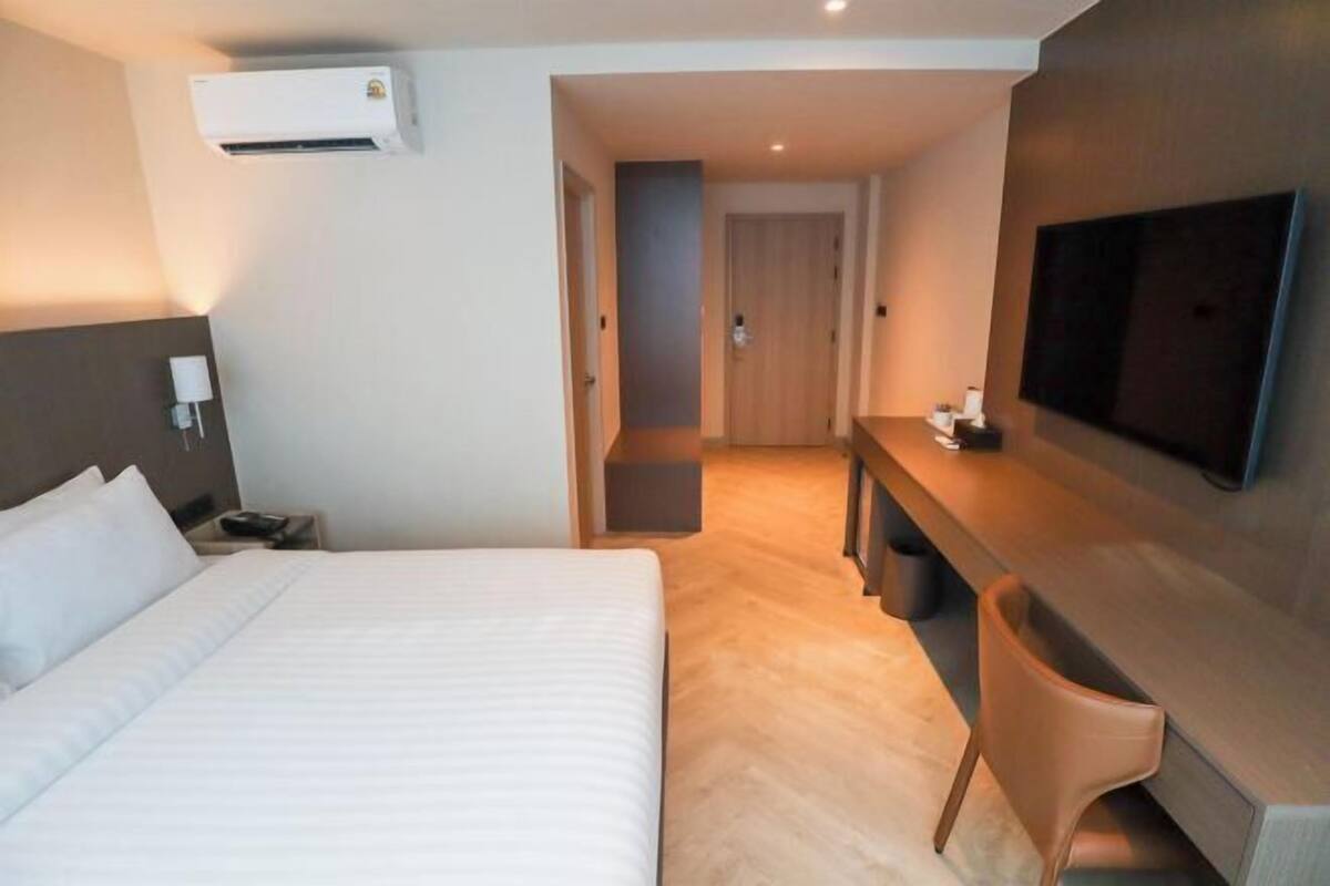 Una habitación de hotel con cama, escritorio, silla, televisor y aire acondicionado.