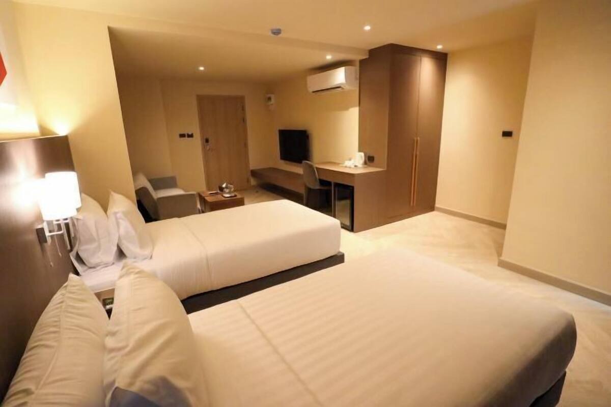 Habitación de hotel con dos camas, un escritorio, una silla, un televisor y un armario.