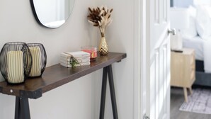 Una sala de estar moderna con una consola de madera oscura, un espejo, jarrones decorativos y una pequeña planta.
