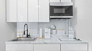 Una cocina moderna con armarios blancos, un lavamanos de acero inoxidable, un microondas y una cafetera.