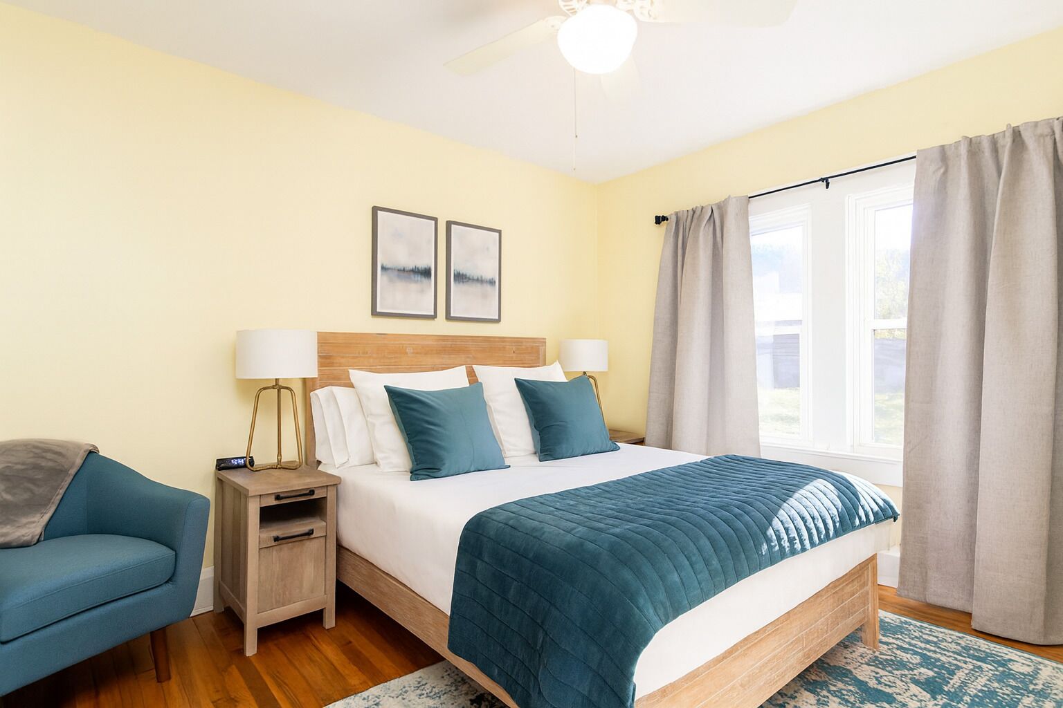 A hotel room with a bed, bedside tables, a chair, and a window with curtains.