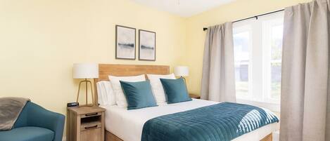 A hotel room with a bed, bedside tables, a chair, and a window with curtains.
