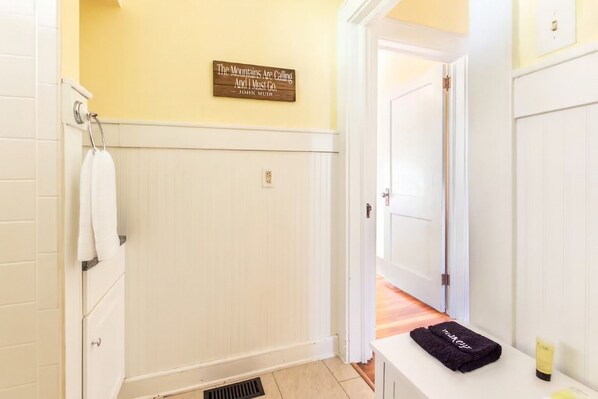 A bathroom with a white vanity, a towel rack, a sign on the wall, and a door leading to another room. - Private Mountain Cottage with Hot Tub, Fire Pit, and Fenced Yard Near Asheville (Mars Hill)