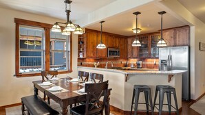 A kitchen with wooden cabinets, a stainless steel refrigerator, and a dining area with a table set for four. - Downtown Winter Park Area Condo H-201 I Great Views I Bunk Room I Discounted Attractions (Fraser)
