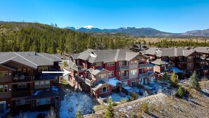 A multi-story residential building with balconies and a view of snow-capped mountains in the background. - Downtown Winter Park Area Condo H-201 I Great Views I Bunk Room I Discounted Attractions (Fraser)