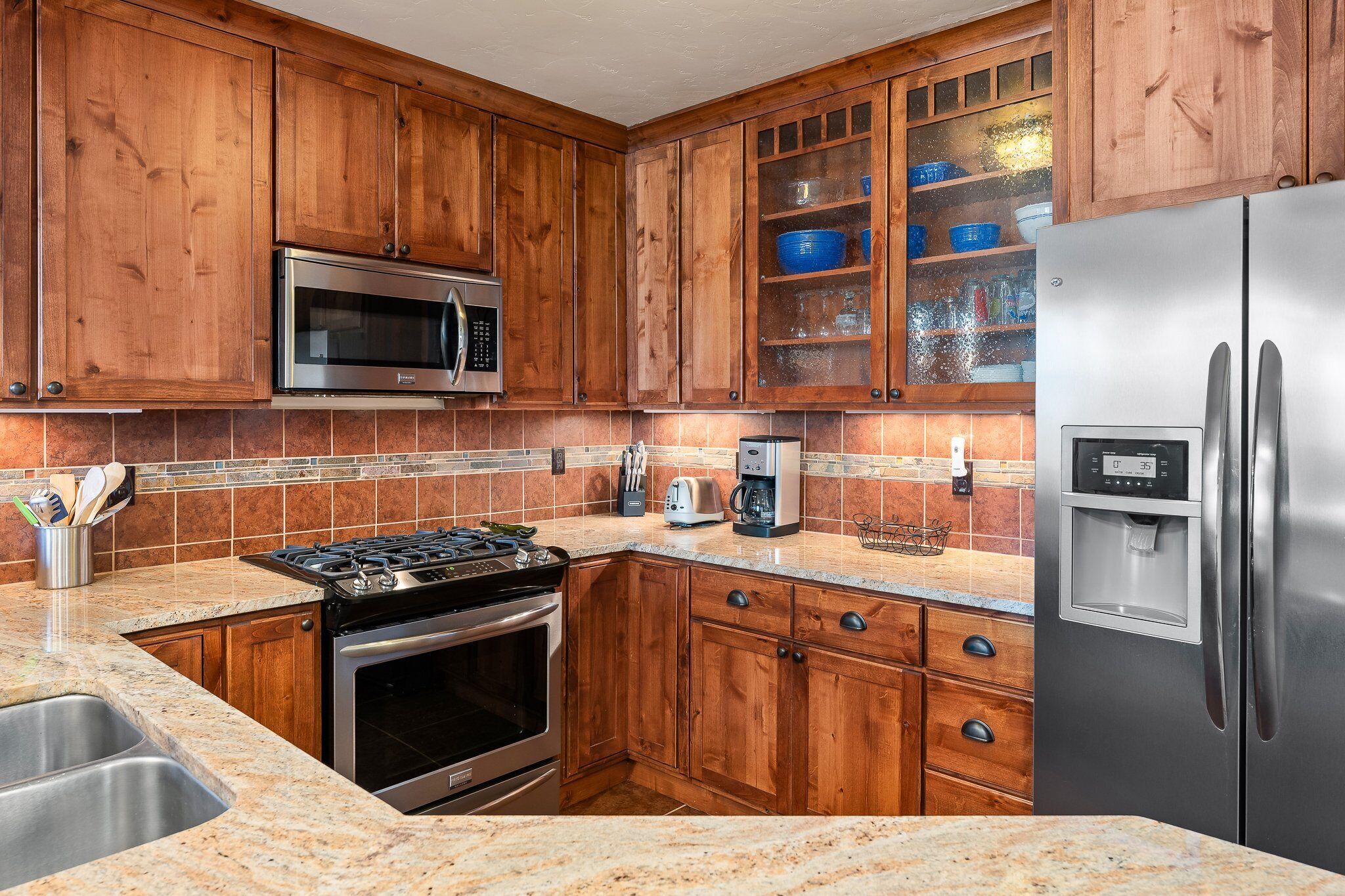 A kitchen with wooden cabinets, a stainless steel refrigerator, a microwave, a stove, and a coffee maker.