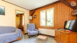 Et hyggeligt rum med trælofter, en sofa, en lænestol, et lille bord, et fjernsyn og et vindue med gardiner.