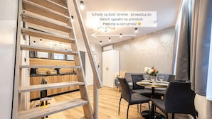 A modern interior with a wooden staircase, a dining area with grey chairs, and a kitchen visible in the background. - Family Loft With Mezzanine Old Town (Torun)