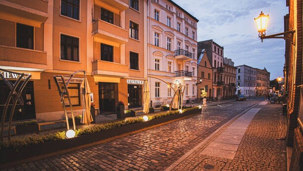 A cobblestone street lined with historic buildings, some with visible signage. - Family Loft With Mezzanine Old Town (Torun)