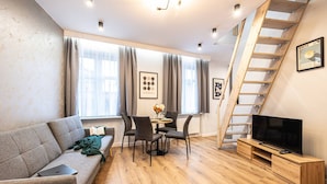 A modern living room with a sofa, dining table, chairs, a TV, and a wooden staircase. - Family Loft With Mezzanine Old Town (Torun)