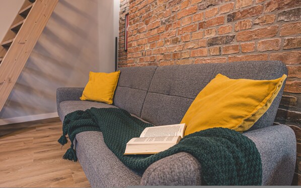 A grey sofa with two yellow pillows, a green blanket, and an open book. - Estrella 14 - Loft z Dusz w Centrum Toru Skiej Star wki (Torun)