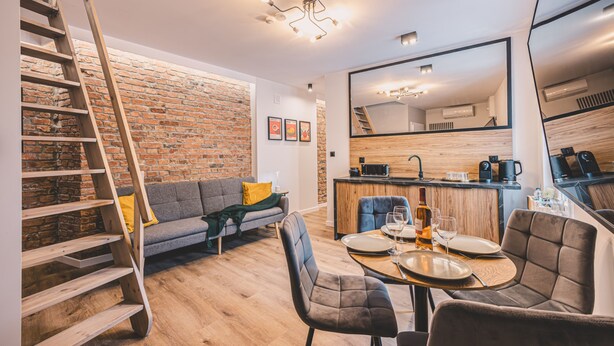 Un appartement moderne doté d’une cuisine de style industriel, d’un coin repas et d’un salon avec un mur en briques et un escalier.