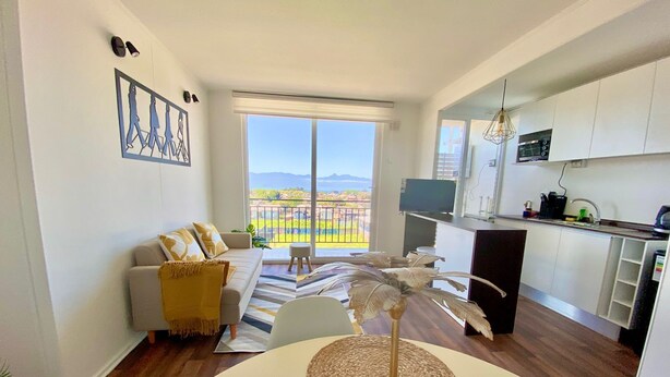 A modern apartment with a balcony, a living area with a sofa, a dining table, and a kitchen with white cabinets. - Beautiful apartment with excellent volcano and lake view. (Villarrica)