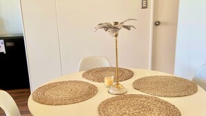 A round dining table with woven placemats, white chairs, and a decorative metal stand with a plant. - Beautiful apartment with excellent volcano and lake view. (Villarrica)