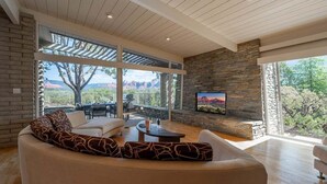 A modern living room with a stone fireplace, large windows, and a comfortable seating area. - New Listing Vast Red Rock Views 2 Master Suites - Panorama Landing (Sedona)