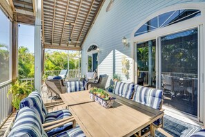 En overdækket terrasse med et træbord og stribede sofaer, omgivet af glasdøre og -vinduer.