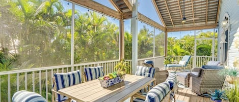 A covered outdoor area with a wooden table, striped seating, and potted plants.