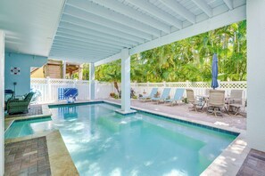 A covered swimming pool with lounge chairs and a view of tropical vegetation. - Griffins' Island Getaway (Holmes Beach)