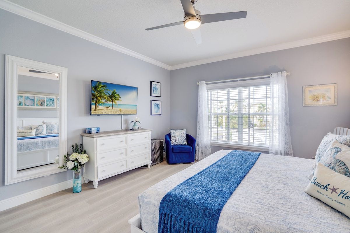 A bedroom with a bed, a dresser, a chair, a window with curtains, and a ceiling fan.