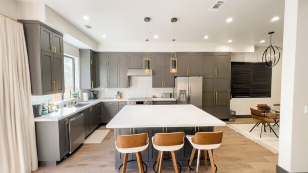 Une cuisine moderne dotée d’un grand îlot central, de meubles de couleur gris foncé, d’appareils électroménagers en acier inoxydable et de luminaires suspendus.