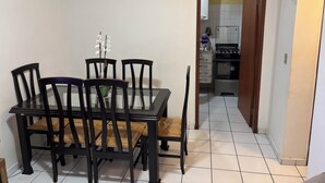 A dining area with a glass table and wooden chairs, a small potted plant, and a kitchen visible through an open doorway. - 2-Bedroom Apartment Near Ouro Minas Hotel (Belo Horizonte)