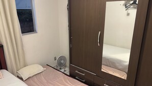 A bedroom with a bed, a wardrobe, a mirror, and a fan. - 2-Bedroom Apartment Near Ouro Minas Hotel (Belo Horizonte)