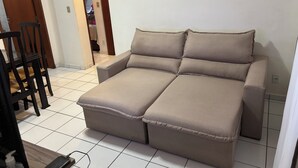 A beige sofa with a wooden frame, a dining table with chairs, and a tiled floor. - 2-Bedroom Apartment Near Ouro Minas Hotel (Belo Horizonte)