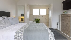 Un dormitorio con cama, mesitas de noche, cómoda, televisor y baño con ventana.