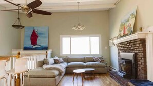A living room with a sectional sofa, a fireplace, a window, and a ceiling fan. - Manchester by the Sea l Fireplace l King Bed (Manchester-by-the-Sea)