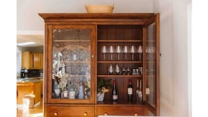 A wooden cabinet with glass doors, containing various bottles and glassware. - Manchester by the Sea l Fireplace l King Bed (Manchester-by-the-Sea)