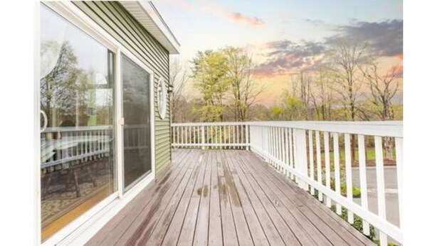 A wooden deck with a white railing, a glass door, and a view of trees and a sunset. - Manchester by the Sea l Fireplace l King Bed (Manchester-by-the-Sea)