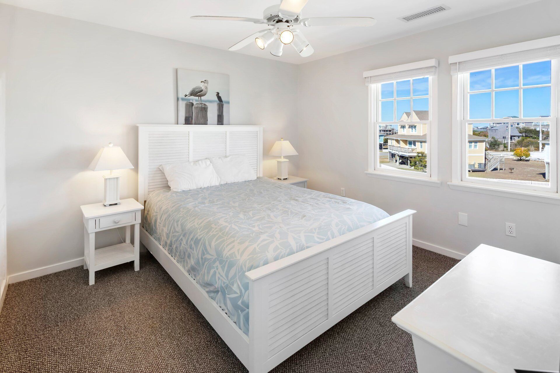 A bedroom with a bed, two bedside tables with lamps, a ceiling fan, and a window with a view of buildings.