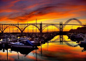 A marina with boats docked, a bridge in the background, and a sunset.