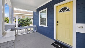 Una casa con puerta amarilla, porche blanco y pared exterior azul.