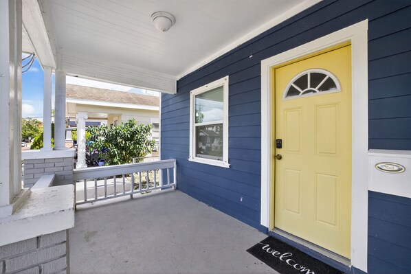 A house with a yellow door, a white porch, and a blue exterior wall.